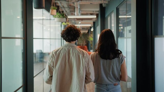 Rear view of young couple walking to office along corridor of modern open plan building shot in slow motion