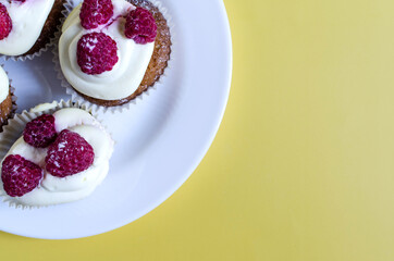 Homemade cupcakes with cream and berries on a white plate on a colored background. Cakes cupcake on a colored background top view place for text.