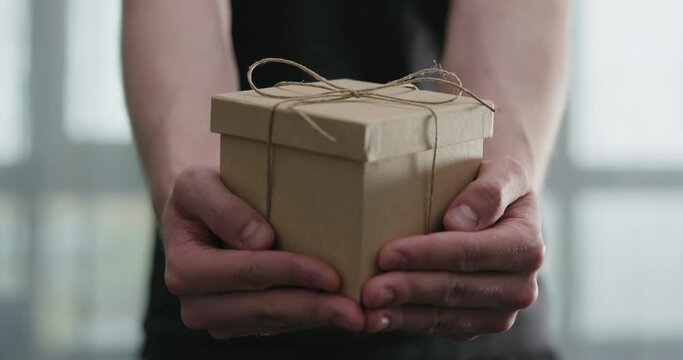 Slow motion young man shows brown craft paper gift box