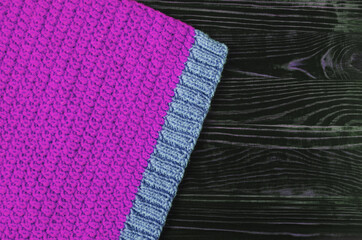 A fabric knitted from lilac and blue threads on a dark wood background, a top view of the mine space. The texture of the knitted fabric