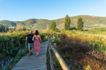Man and woman walking along a wooden walkway surrounded by nature on a sunny morning. 
