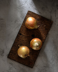 Onions on an old wooden board on a concrete background in the rustic style. Top view