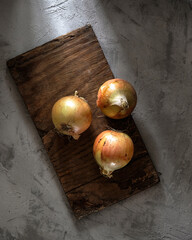 Onions on a rectangular wooden board on a concrete background in the rustic style. Top view