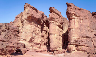 Fototapeta premium tiny tourists looking up at the majestic Solomons Pillars sandstone formation in Timna Park in Israel with a clear blue sky background