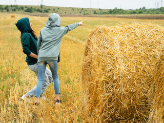 Naklejka na ściany i meble Adorable, happy teenage girl and girl having fun on a wheat field on a summer day. Laugh in a field of hay bales during harvest and enjoy the warm day outdoors.