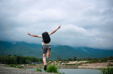 Fototapeta premium Back view point of young man backpacker jumping over the ground and raising his arm with victory sign , freedom , inspiration and motivation concept