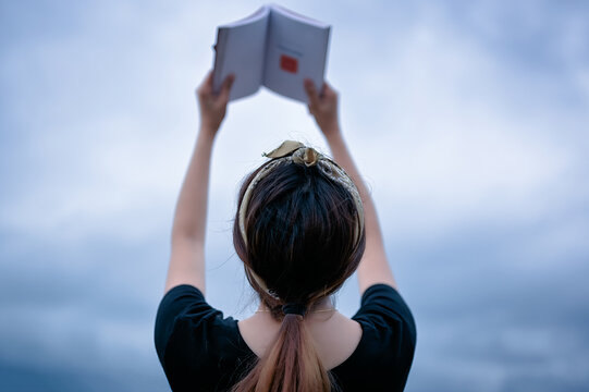 Back view point of young women raising the book in her hand , growth , learning and wisdom concept