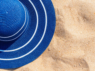 Horizontal photo: blue straw hat on golden sand at the beach, copy space for text. Sea vacation concept.