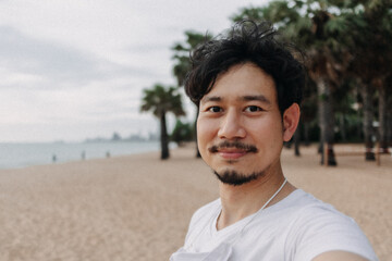 Happy Asian man take selfie with palm tree on the beach. Summer travel concept.