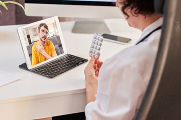 Obraz na płótnie Canvas A woman doctor prescribes pills to a patient through an internet medical consultation