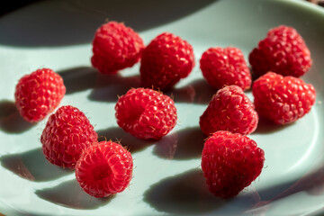 Ripe raspberries on a plate of turquoise color. Closeup. Focus on foreground. Summer advertising background of fresh raspberries on turquoise background, desserts and drinks made from raspberries