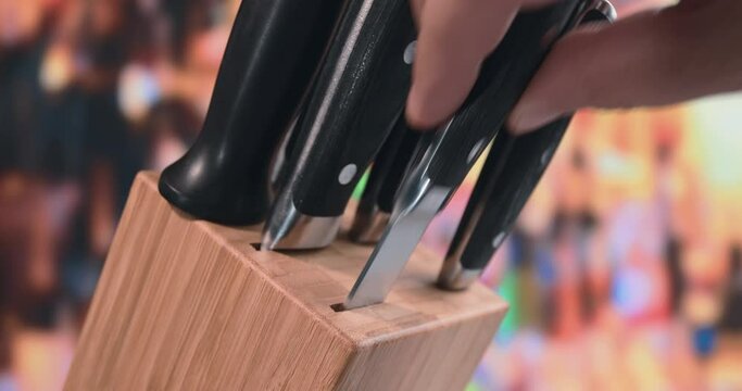 The man takes out two knives in turn from a wooden stand. He looks at each knife for a few seconds and inserts it back into place. A man's hand holds a knife. A set of knives for the kitchen.