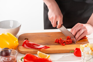 Hands cutting red pepper into fine dice on a wooden board