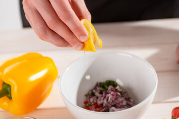 Hand squeezing lemon juice into a bowl with freshly cut ingredients