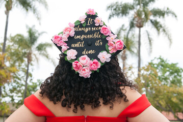 Grad girl wearing a graduation cap decorated with pink flowers and golden letters. 