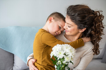 Tender son kisses the happy mother and gives her a bouquet of flowers, congratulating her on mother's day during holiday celebration at home. Family holidays and celebration concept