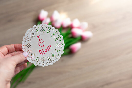 a bouquet of pink tulips on a wooden background and a sign with the words "I love mom"