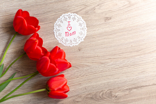 a bouquet of red tulips on a wooden background and a sign with the words "I love mom"