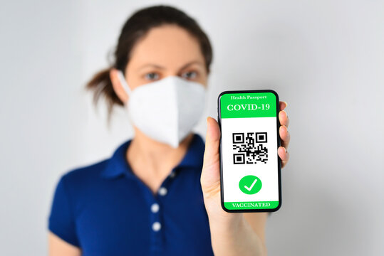 Defocused young girl wearing a face mask, holding a smartphone with a Green Pass. The Green Pass facilitate the safe free movement within the EU. Health Passport concept. Focus on the smart phone.