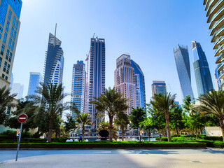 Skyscrapers at the Dubai Marina and park with blue sky, view from the street
