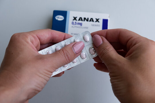 Tallinn, Estonia - July 16, 2021: Woman taking Xanax tablet by Pfizer for treating panic and anxiety disorder. Package of pills. Pharmacy and medicine concept.