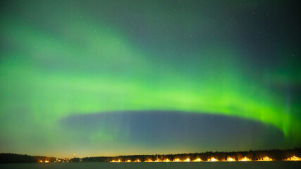 A green colour Aurora borealis panorama on the starry night sky over a city. Aurora Borealis over Swedish lake Islands. Northern Sweden.