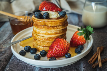 Closeup view of Stack of pancakes with honey stick, strawberry, blue berry and whip cream on top in plate, delicious dessert with milk