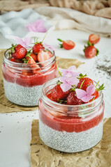 Healthy strawberry fruit dessert with milk and chia seeds in jar on light background. Healthy raw vegetarian dessert.