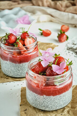 Healthy strawberry fruit dessert with milk and chia seeds in jar on light background. Healthy raw vegetarian dessert.