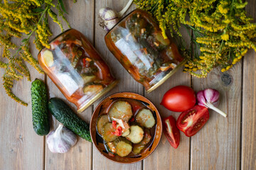 Preservation: spicy cucumbers with garlic in tomato sauce in jars on a wooden table. Top view