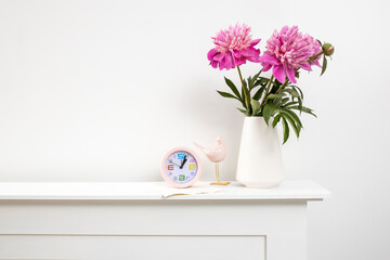 Red, pink peonies in a white vase on a table, clock, and against a white wall background