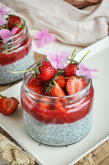 Healthy strawberry fruit dessert with milk and chia seeds in jar on light background. Healthy raw vegetarian dessert.