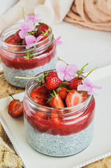 Healthy strawberry fruit dessert with milk and chia seeds in jar on light background. Healthy raw vegetarian dessert.