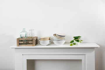 Fototapeta na wymiar kitchen utensils, cups, bowls, bottles, storage items, artificial monstera in a ceramic pot are on a white dresser