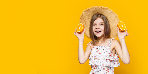 Happy little girl in a straw hat holding an orange on a yellow background with space for text.