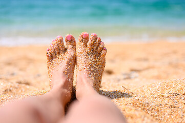 Beautiful legs of a young girl with adhered large sand against the background of the sea. The concept of a good seaside vacation