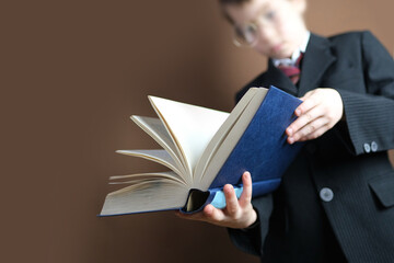 smart child 7-8 years old, kid in black school suit stands and reads thick tome, open paper book,...