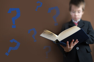 smart child 7-8 years old, kid in black school suit stands and reads thick tome, open paper book...