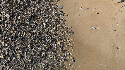 Beach sand with small stones and sea foam in beautiful coast