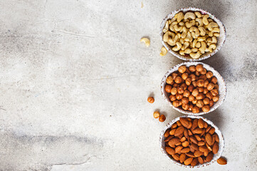Top view of three bowls with shelled hazelnuts, cashew and almonds on concrete background with copy space