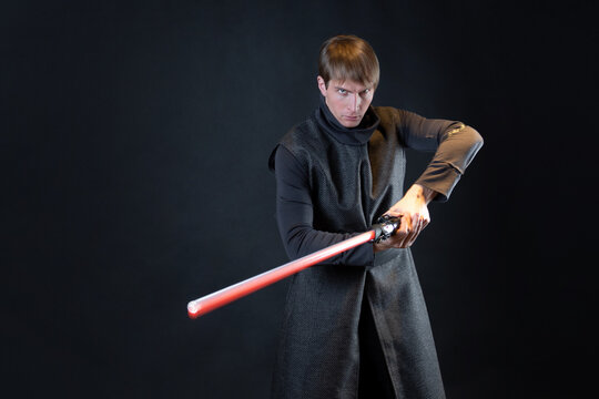 A villain with a red lightsaber, a young man in a long robe does fighting poses,