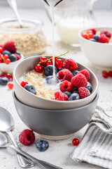 Milk oatmeal porridge with fresh raspberries and blueberries. Pouring milk. Healthy breakfast. Vegetarian food. Selective focus 