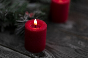 Close up of single red glowing candle with fir and wood dark background for a merry Christmas or happy New Year celebration concept