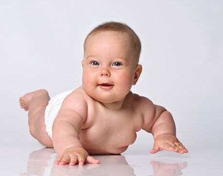 Little cute naked baby in a diaper smiles and crawls on all fours on a white background in the studio. A joyful little child is looking at you. Isolated.