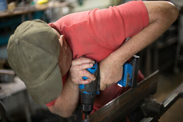 A man drills holes in the metal. The guy works in the workshop.