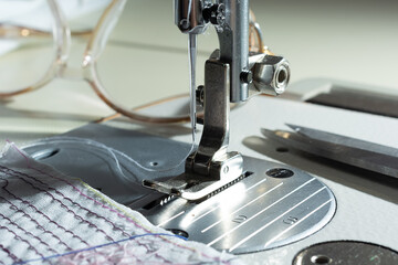 close-up of mechanism with a needle of an electric sewing machine. against the background of glasses and fabric with threads