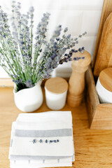 kitchen details, vase with lavender flower and towels on wooden table, white ceramic brick wall background. Sustainable living eco friendly kitchen.