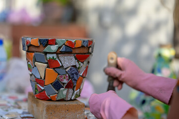 Older people decorate earthenware with mosaic techniques in the master class or in the fresh air in the workshop. Homemade mosaic flower pot with porcelain pieces.