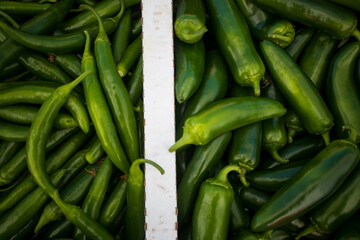 Two varieties of organic green chili peppers - Jalapeño and Serrano, in a box at a market in...