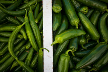 Two varieties of organic green chili peppers - Jalapeño and Serrano, in a box at a market in California